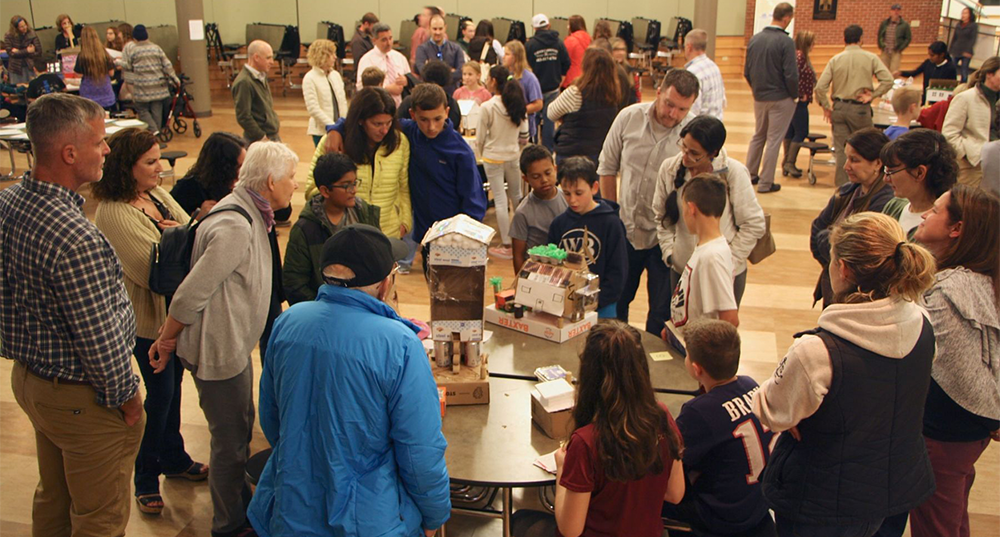 Parents visit their children's booths in a school cafeteria as they present as part of the Climate in the Classroom program.