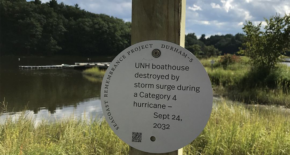 A sign along the Oyster River reads "UNH Boathouse destoryed by storm surge during a Category 4 huricane - September 24