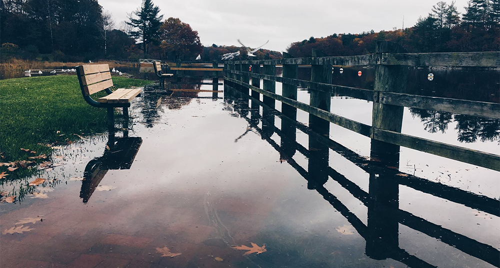 High tide under a fence and bench at the Durham Town Landing on a gloomy day during a King Tide