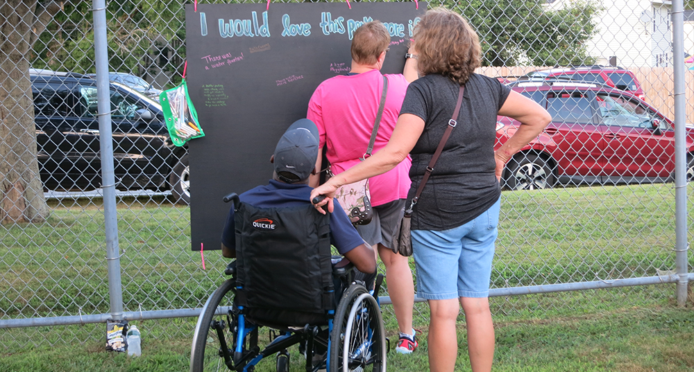 Three adults gather around an interactive chalkboard display to answer, "what would make this park even better?"
